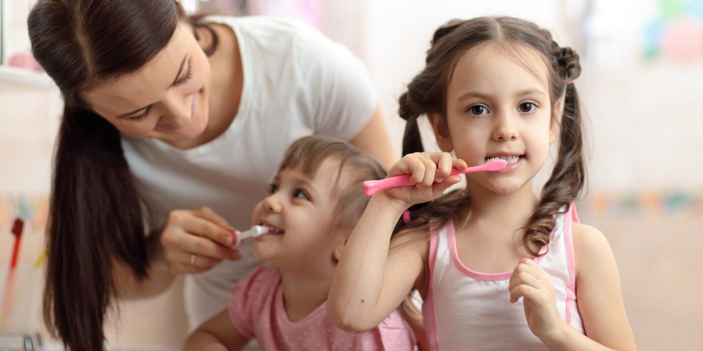 Come lavare i denti ai bambini: nell'immagine due bambini con la mamma durante il lavaggio dei denti