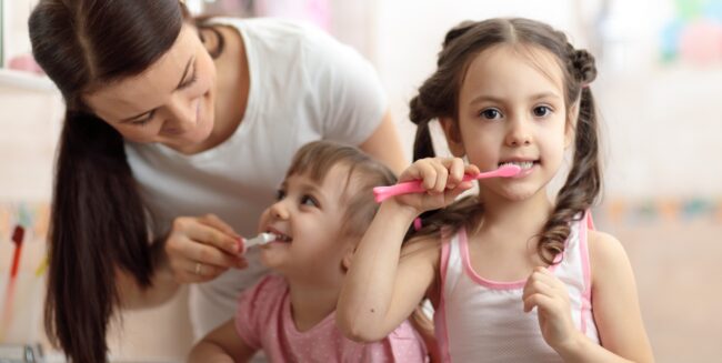 Come lavare i denti ai bambini: nell'immagine due bambini con la mamma durante il lavaggio dei denti